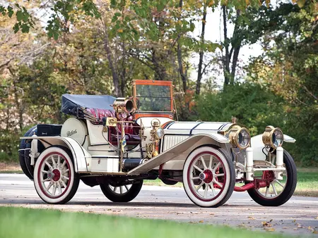 1912 Packard Six Vintage convertible car with a white body color, with white colored wheels, parked on concrete with trees in the background