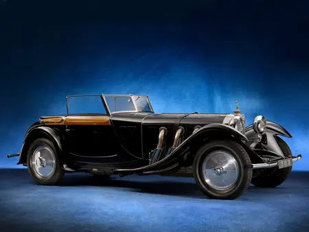 Black 1928 Mercedes Benz with silver plate rims, parked inside a showroom with blue background carpet and curtains