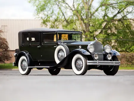 Black 1930 Packard Deluxe Vintage Car with silver rims and white accent, on concrete with a tree in the background