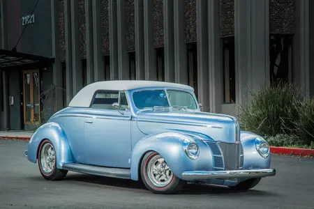 Light Blue 1940 Ford convertible white small light blue wheels, parked on the road with part of a building in the background