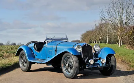 Blue 1932 Alfa Romeo Vintage convertible with black wheels, parked on asphalt with bare trees in the background