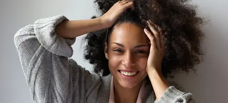 Curly haired Woman Smiling at camera with both hands touching her hair