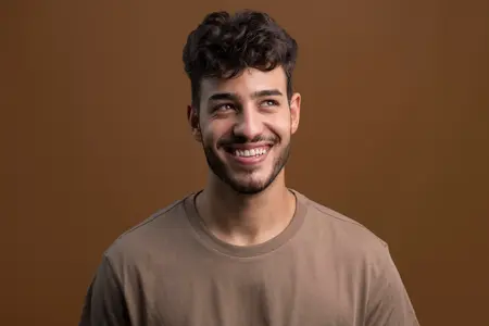 Man in a brown shirt smiling looking up and to the right with a brown background